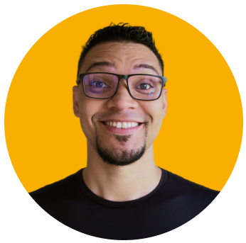 Foto de Mayk Brito sorrindo, usando óculos e uma camiseta preta, barba e fundo amarelo.